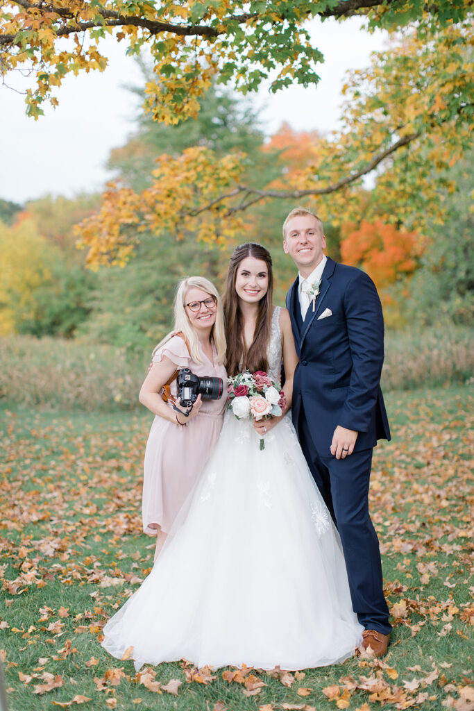 a bride and a groom with their wisconsin wedding photographer standing in fall leaves showcasing a gift of friendship